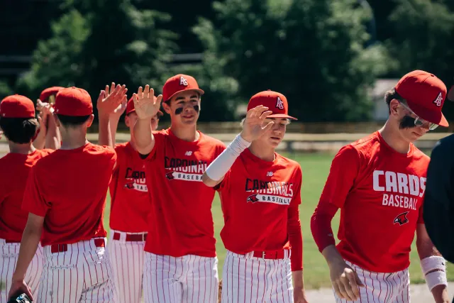 Cardinals players in red club shirts and pinstripe pants high-five their way down the line after a game.